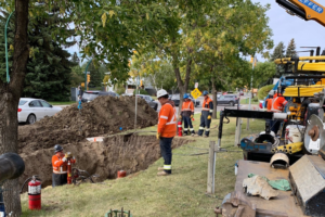 Photo of a crew wearing MWG FR Clothing. Workers are wearing bright orange tops with silver segmented reflective tape on torso and sleeves to meet high-visibility standard CSA Z96-15. Workers are wearing FR Clothing because they are working in a hazardous environment.